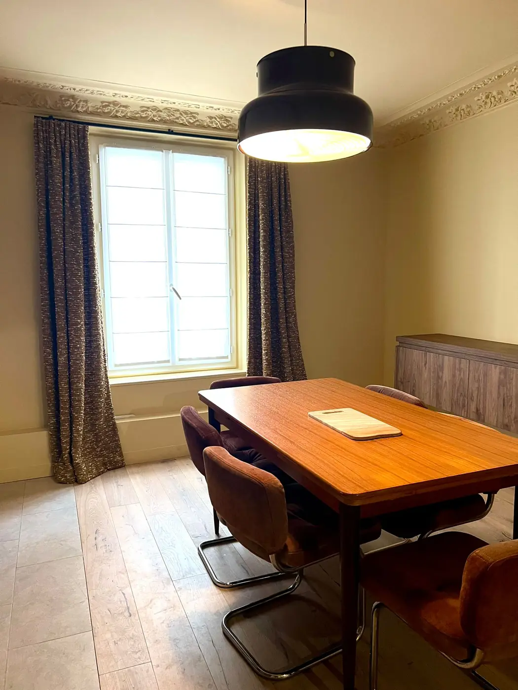 Salle à manger rénovée avec suspension noire et parquet clair dans un appartement haussmannien à Paris 9e