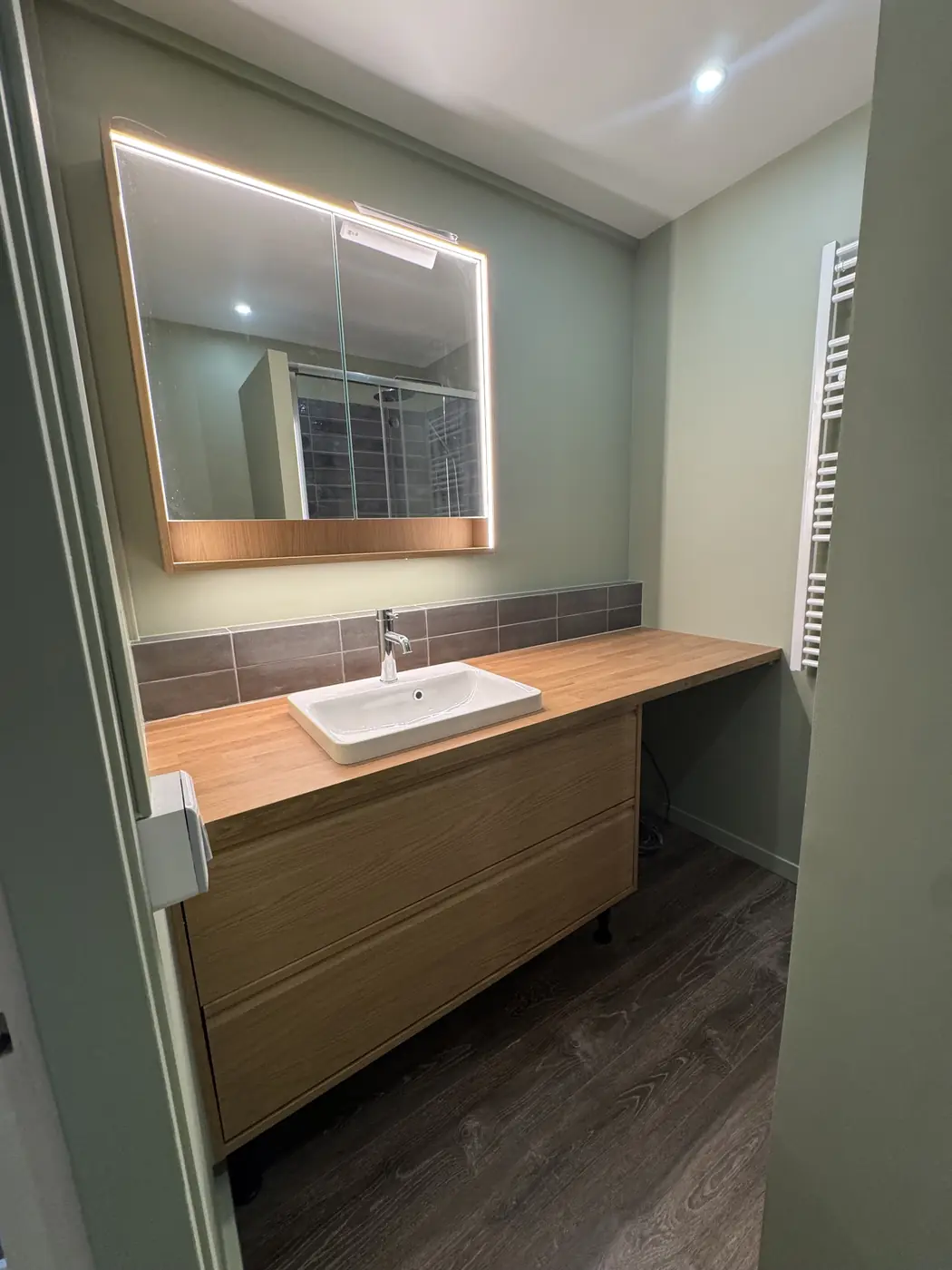 Salle de bains vert sauge, meuble vasque bois et miroir lumineux, Paris 13e